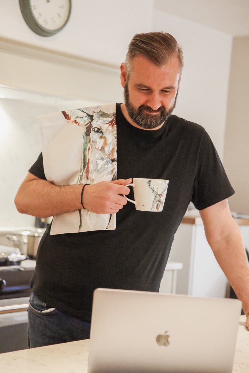 Man holding a mug in a kitchen with a laptop on a counter
