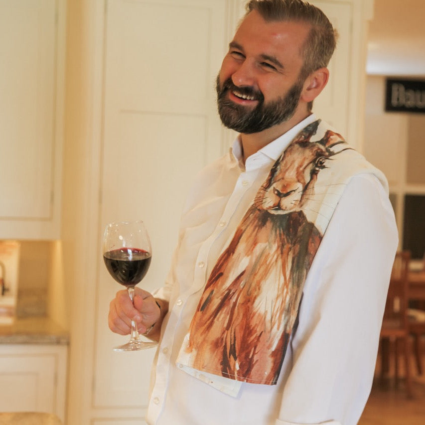 Man in a kitchen holding a glass of red wine, wearing a sweater with a cat design.
